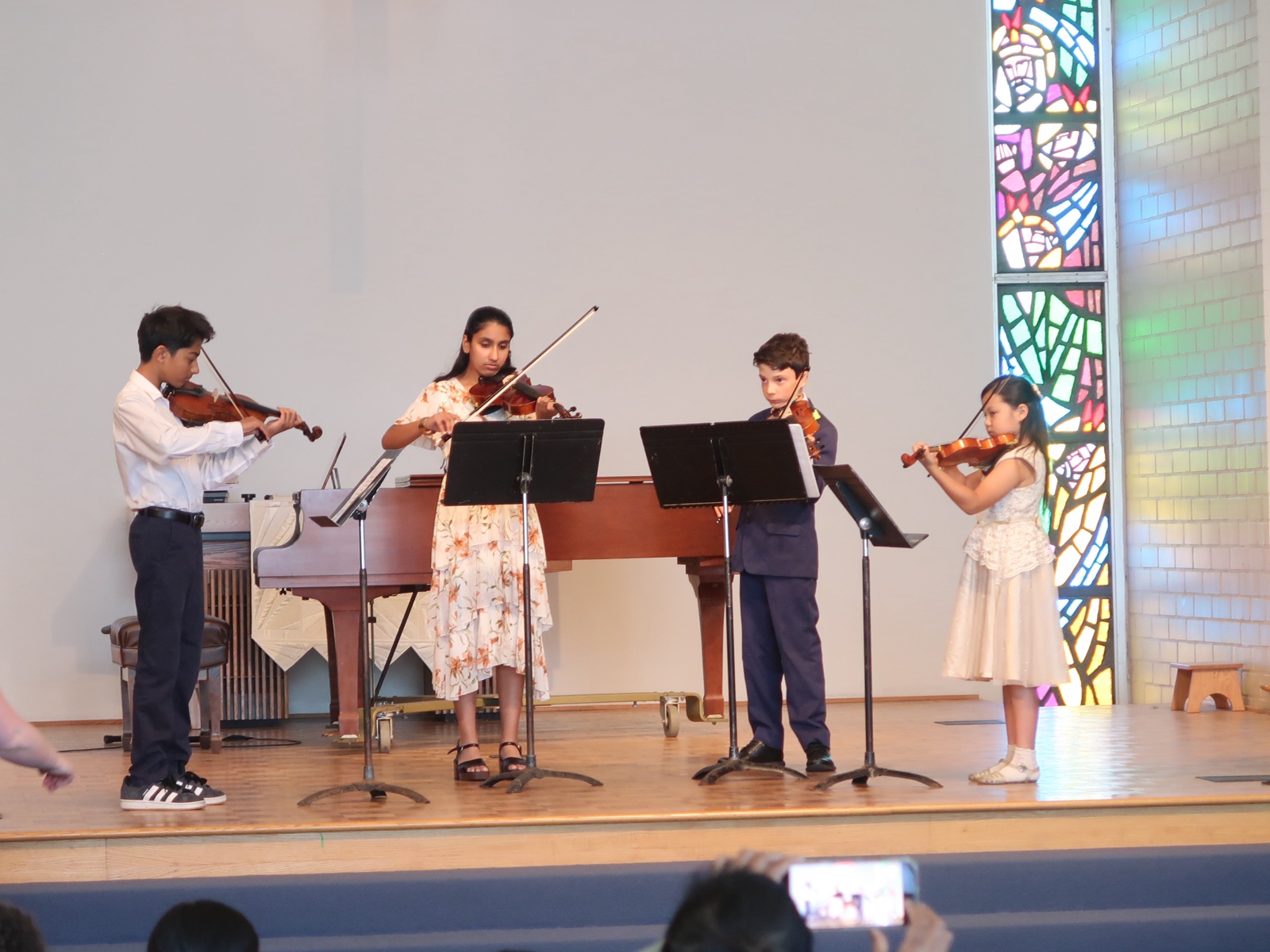 Four young violinists performing together on stage